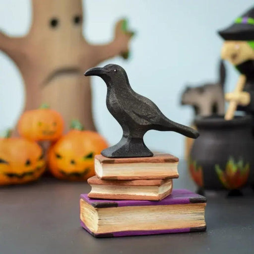 BumbuToys Wooden Halloween Black Raven Bird Figurine on Spooky Books in Small World Play Scene with Pumpkins and Witch with Cauldron in the Background