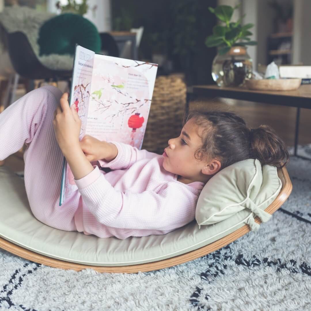 Child relaxing on her Wobbel Board with cosy fabric Wobbel Deck and Pillow - an inviting playroom reading nook, at Oskar's Wooden Ark in Australia