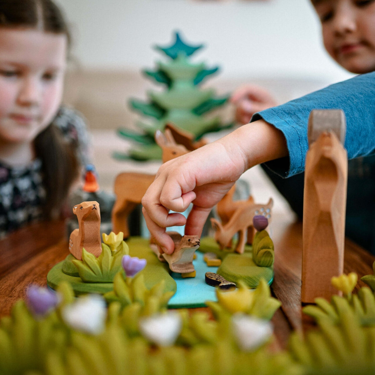Children engaged in imaginative small world play - a woodland scene incorporating Bumbu handcrafted wooden animals and trees, available in Australia from Oskar's Wooden Ark
